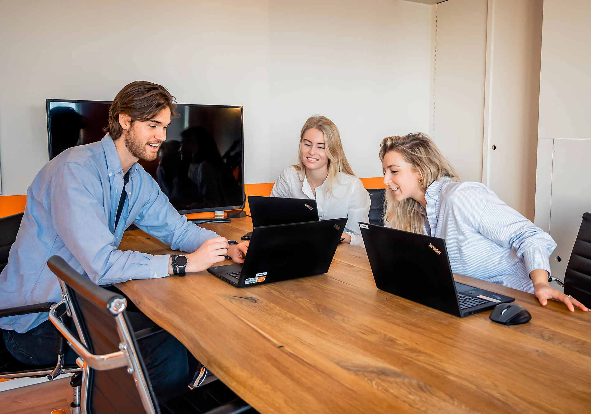 Drie jonge professionals rond een vergadertafel met laptops.