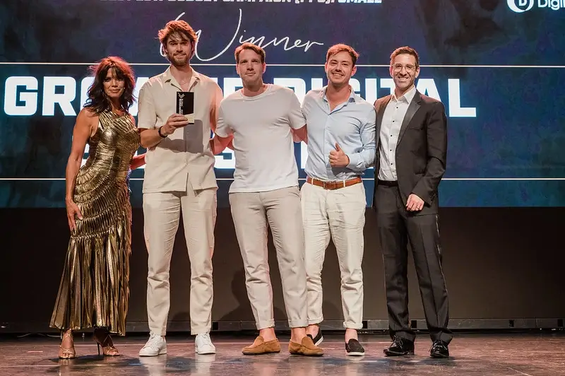Job knipscheer en Peter Maas poseren op een podium tijdens een prijsuitreiking van de Dutch Search Awards. De tweede persoon van links houdt een trofee vast. Ze staan voor een scherm met de tekst: “Winner” en “GROW UP DIGITAL.”